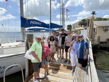 A cheerful group poses for a photo on the dock next to the sailboat 'Phoenix' — perfect for family gatherings and memorable boating adventures.