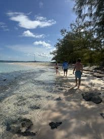 A group of friends strolls along a picturesque beach with a sailboat anchored in the background, capturing the essence of island hopping adventures.
