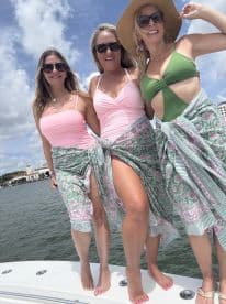 Three friends pose joyfully on the bow of a boat, showcasing their summer swimwear and enjoying a sunny day on the water — perfect for memorable outings and celebrations.
