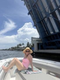 A woman relaxes on the deck of a boat as it passes under a raised bridge, enjoying a sunny day on the waterway.