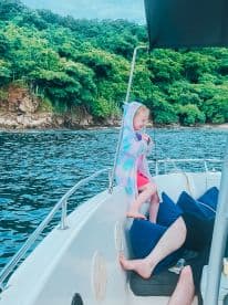 A joyful child plays on the deck of a boat, capturing the essence of family fun on the water amidst lush greenery.