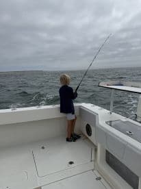 A young child enjoys fishing from the deck of a boat, capturing the joy of a family fishing trip on the open ocean.