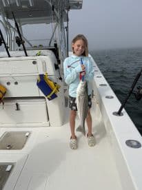 A young girl proudly holds her catch of the day while fishing on a boat, showcasing the joy of family fishing trips and outdoor adventures.