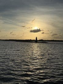 A stunning sunset casts a golden glow over the water, highlighting a lighthouse in the distance — a picturesque scene perfect for evening boat trips.