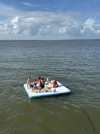 A lively group enjoys a sunny day on a floating mat in the water, perfect for summer fun and relaxation.