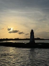 A picturesque sunset view featuring a lighthouse silhouetted against the colorful sky, with a person standing nearby, creating a serene coastal atmosphere.