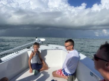 Two children enjoy a sunny day on a boat, surrounded by beautiful ocean views and dramatic clouds — a perfect moment of fun on the water.