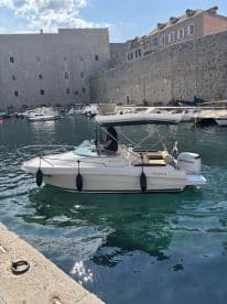 A sleek speedboat is seen navigating the calm waters of a picturesque harbor, surrounded by historic stone buildings — perfect for exploring coastal destinations.