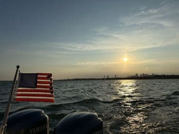 A picturesque sunset view from a boat, showcasing the American flag and the city skyline in the background — perfect for evening cruises on the water.