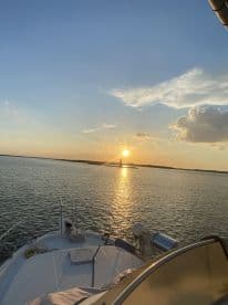 A serene sunset view from the bow of a boat, showcasing the tranquil waters and a distant lighthouse, perfect for evening cruises.