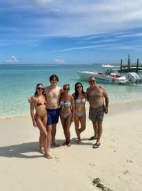 A cheerful group poses on the beach with a boat in the background, capturing a perfect day of fun and relaxation by the water.