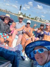 A joyful group of family and friends poses for a fun photo on a boat, with a lighthouse in the background — capturing the essence of a memorable day on the water.