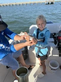 A young girl proudly holds her catch while fishing on a boat, showcasing a memorable family experience on the water.