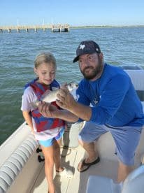 A young girl and an adult proudly display their catch while fishing on a boat, capturing a memorable moment of family fun on the water.