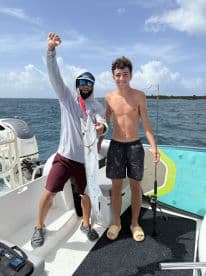 A young angler proudly displays his catch alongside a fishing guide on a boat, showcasing the thrill of fishing adventures on the water.