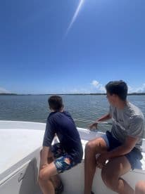Two boys enjoy a scenic boat ride, gazing at the beautiful water and sky — a perfect moment for family adventures on the water.