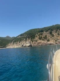 A scenic view of a boat navigating along a stunning coastline, showcasing the beautiful blue waters and lush greenery of the surrounding landscape.