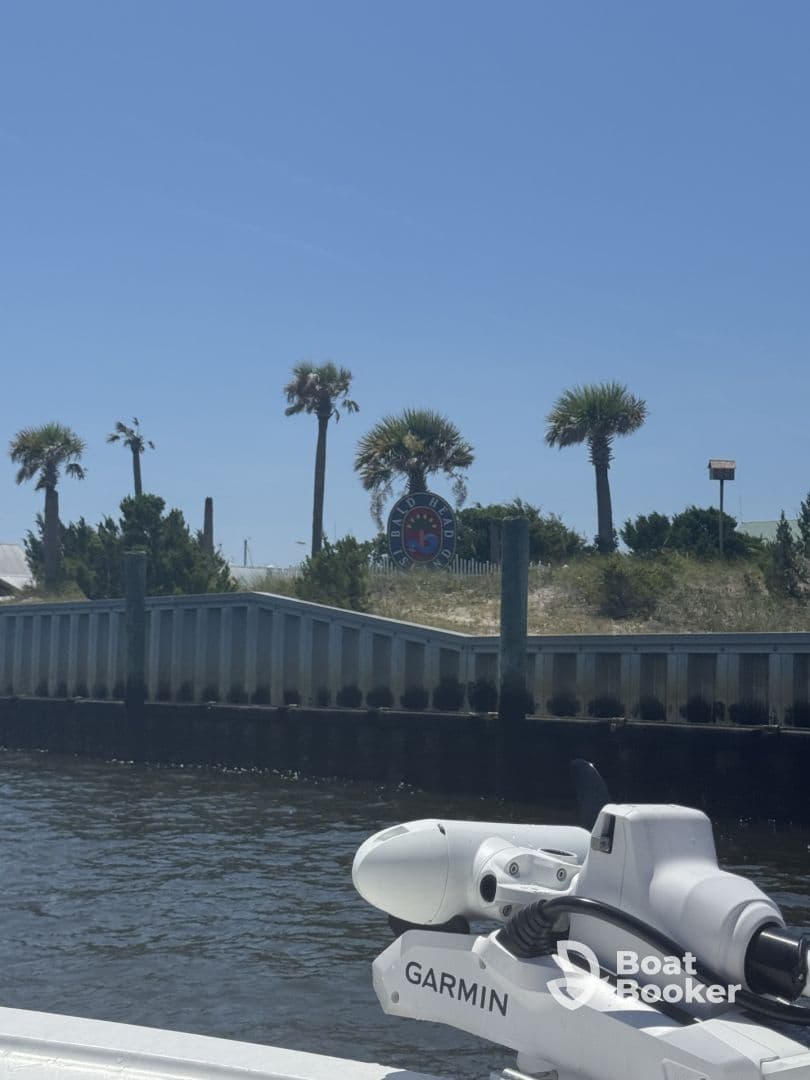 An unclear view of a boat's equipment with a distant shoreline featuring palm trees and a sign, lacking focus on any specific subject.