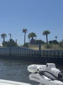 An unclear view of a boat's equipment with a distant shoreline featuring palm trees and a sign, lacking focus on any specific subject.