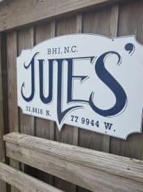 A close-up of a sign for 'Jules' located in BHI, N.C., featuring geographical coordinates. Ideal for identifying local attractions.