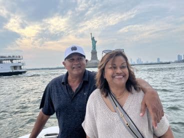 A happy couple poses for a photo on a boat tour near the iconic Statue of Liberty, capturing a memorable moment against a stunning skyline backdrop.