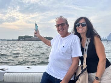 A couple enjoys a scenic boat tour with the Statue of Liberty in the background, capturing a memorable moment on the water.