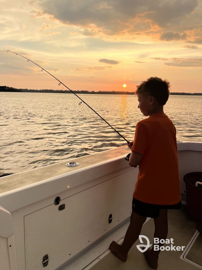 A child enjoys fishing from a boat at sunset, creating a serene and memorable moment on the water.