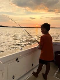 A child enjoys fishing from a boat at sunset, creating a serene and memorable moment on the water.