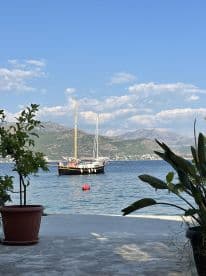 A picturesque view of a sailboat docked in calm waters, framed by lush greenery and mountains in the background — an ideal setting for a relaxing day by the sea.