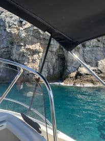 A close-up view of the helm area on a boat, showcasing the console and shade, with a stunning rocky coastline in the background.
