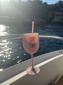 A stylish pink cocktail glass with 'GRL PWR' sits on the edge of a boat, capturing the essence of relaxation and fun on the water.