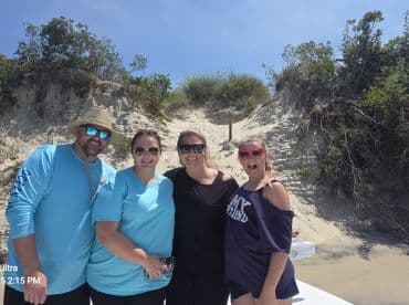 A cheerful group of friends poses for a photo on the beach, capturing a fun moment during their boating adventure.