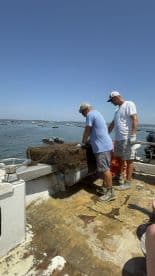 Two crew members work on a fishing boat, preparing equipment while surrounded by a scenic ocean view — a glimpse into the fishing experience on the water.