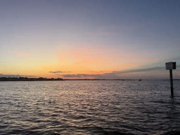 A stunning sunset over the water, showcasing vibrant colors and a serene coastline — perfect for capturing the beauty of evening boat trips.