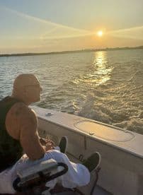 A man enjoys a tranquil sunset on a boat, sipping a drink and taking in the serene waterscape — an ideal moment for relaxation and reflection.