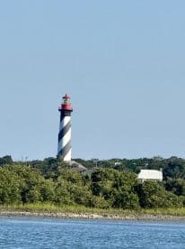 A scenic view of a lighthouse standing tall against a clear blue sky, surrounded by greenery — a picturesque landmark often seen from the water.