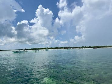 A picturesque view of multiple boats anchored near a sandy beach, with people enjoying the clear waters — perfect for island hopping adventures.