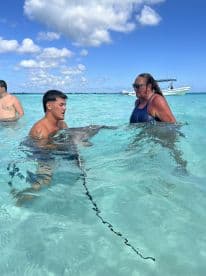 Two individuals interact with a stingray in shallow waters, showcasing a unique wildlife experience in a tropical setting.
