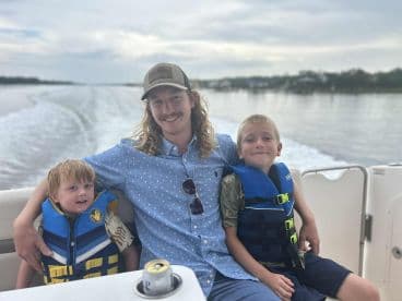 A joyful moment on the water with a father and his two young sons, all wearing life jackets, enjoying their time aboard a boat.