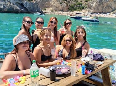 A vibrant group of friends enjoys a fun day on the water, celebrating with drinks and laughter against a stunning beach backdrop.