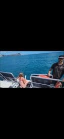 A child sits on the edge of a boat while an adult stands nearby, enjoying a sunny day on the ocean — a perfect moment for family fun and adventure.