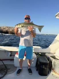 A proud angler holds up a freshly caught striped bass aboard a boat, showcasing the thrill of fishing on the open water.