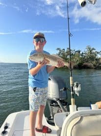 A young angler proudly holds up his catch aboard a fishing boat, showcasing the excitement of a successful day on the water.