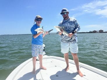 A child and an adult proudly display their catch of the day, holding sharks while fishing on a boat — a thrilling experience for young anglers.