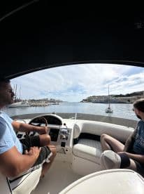 Two individuals enjoy the helm of a boat, navigating through a scenic harbor — perfect for exploring coastal destinations.
