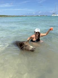 A woman enjoys a unique experience swimming with a friendly pig in crystal-clear waters, showcasing a memorable wildlife encounter in the Bahamas.