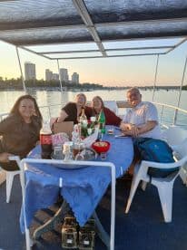 A cheerful group enjoys a sunset cruise on a boat, sharing drinks and snacks at a beautifully set table — perfect for gatherings and celebrations on the water.