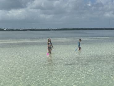 Two children enjoy a fun day at the beach, wading in shallow waters with colorful shovels — a perfect scene for family adventures and beach activities.