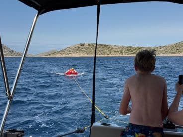 A child enjoys tubing behind a boat while another child watches excitedly — a thrilling on-water activity perfect for summer adventures.