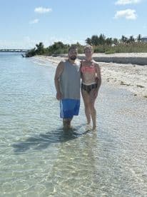 A couple enjoys a sunny day at the beach, standing in shallow water — a perfect moment for a romantic getaway or beach adventure.